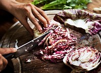 Closeup of hands with knife cutting cabbage on wooden cut board