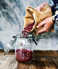 Hands holding sack and pouring beans to the glass jar
