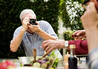 Senior man taking photo of friends with retro film camera