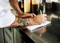 Hand with tattoo writing down an invetory in the kitchen