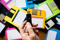 Hand holding USB drive with floppy disk background