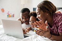 Black family lying on bed using computer laptop together in bedroom