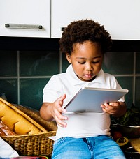 Black kid using digital tablet in the kitchen