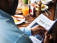 Rear view of black man reading newspaper while having breakfast