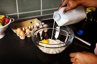 Hand pouring milk to baking flour