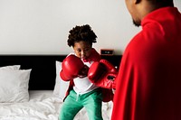 African descent kid wearing robe doing boxing with dad on the bed