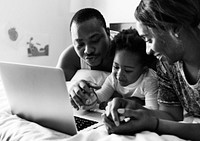 Black family lying on bed using computer laptop together in bedroom