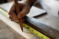 Carpenter using pencil and measurement tape on wood