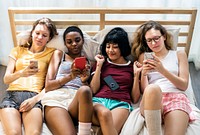 Group of diverse women lying on bed using mobile phones together