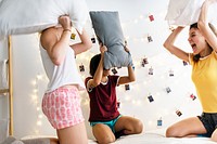 A diverse group of women playing pillow fight on bed together