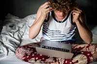 A Caucasian man sitting on the bed using a laptop