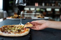 A wine glass and a hand taking a slice of pizza