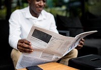 African descent man sitting reading a newspaper outdoor
