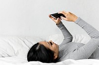 Asian woman lying on bed using mobile phone