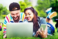 Couple lying down on the grass using laptop