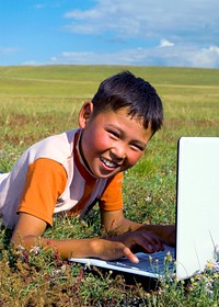 Mongolian boy with laptop on grass.