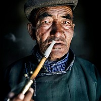 Mongolian man in traditional dress smoking a pipe.