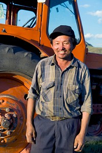 Smiling Mongolian farmer standing next to the tractor.