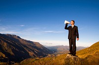 Businessman shouting on the top of the mountain.