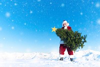 Santa claus carrying a christmas tree on a snow covered mountain.