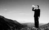 Businessman shouting on the top of the mountain.