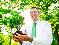 Businessman holding a tree to plant in a forest.