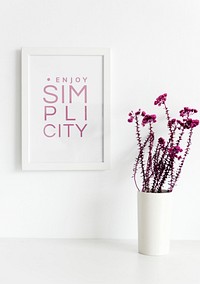 Closeup of pink flowers in white vase with photo frame on wall