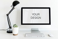 Computer on white table in workspace with black lamp and small plant