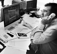 Man talking on the phone looking at stock market analysis on computer screen