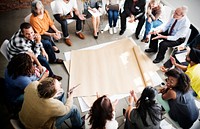 Seated people surrounding a sheet of paper on the floor