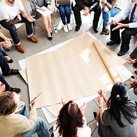 Seated people surrounding a sheet of paper on the floor