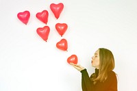 A woman blowing heart balloons