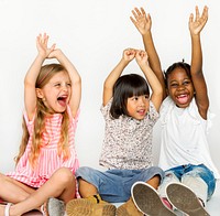 Diverse group of children sitting on the floor hands up