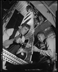 Production. Bombers. High speed bomber production at new plant. Advanced manufacturing methods ensure record output. Fixtures are used in places instead of jigs. Frame section is riveted by the man at the right, while the man at the left bucks up the rivets. Sourced from the Library of Congress.