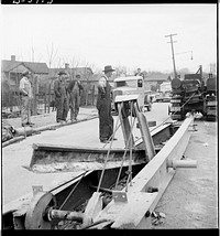 Buried trolley tracks salvaged to aid war program. Removing abandoned trolley tracks to provide much needed scrap for Uncle Sam. Here, in Asheville, North Carolina, a local inventor demonstrates his "railjerk" for doing the trick. He claims his device, employing three men, can pry loose a mile of track a day. Sourced from the Library of Congress.