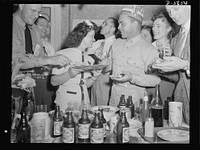 A poster comes to life. Another democratic institution, beer and pretzels. Chief radioman Evans, at extreme left, reached for a slice of the ham which Mrs. Woolslayer is serving. Sergeant Vineyard is wearing the paper hat. Allegheny-Steel, Pittsburgh, Pennsylvania. Sourced from the Library of Congress.