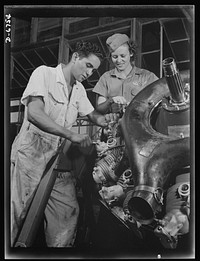 Naval air base. Corpus Christi, Texas. Now an expert mechanic, Mary Josephine Farley shows a National Youth Administration (NYA) trainee the tricks of a Wright Whirlwind motor. He will act as her helper for about eight weeks, then he'll be qualified to work on motors for the naval air base at Corpus Christi, Texas. Sourced from the Library of Congress.