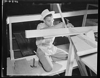 Production. Motor torpedo boats (wooden). An African American carpenter working on the framing of a motor torpedo boat at a large Southern shipyard. These fast seventy-eight-footers are built indoors of prefabricated parts and sections. When the hulls are ready for launching and fitting they are moved from the plant to nearby water. Higgins Industries. Sourced from the Library of Congress.