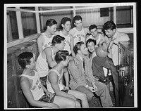 Coach Edwin Firiera, holding ball, gives his near pond team a pep talk in the locker room prior to their first league game. Seated with the players is assistant to the personnel officer at the Pearl Harbor Yard, Harry Brownell. This team is one of those composed of workers in the various shops at the navy yard. Sourced from the Library of Congress.