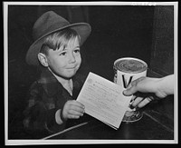 Preparation for point rationing. An eager school boy gets his first experience in using war ration book two. With many parents engaged in war work, children are being taught the facts of point rationing for helping out in family marketing. Sourced from the Library of Congress.