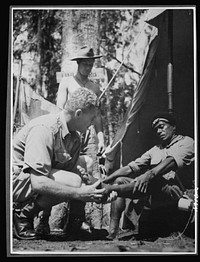 Natives aid Allied drive in New Guinea jungles. New Guinea natives receive the same medical attention as Allied troops, since their work is of vital aid to the Allied forces. Corporal McNicol, medical orderly at one of the forward outposts in the New Guinea jungle, attends one of the native carriers passing through the area. Sourced from the Library of Congress.