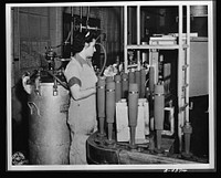 Production. Shell loading. On the "firing line" of a large Midwest loading plant, artillery shells soon to batter the Axis are sprayed with olive drab paint. This women is a sprayer, but women also do the "puddling" of TNT in shells better than men. For "puddling," the stirring and packing of TNT in shells, is done much as a housewife prepares dough for cake. Ravenna ordnance plant. Sourced from the Library of Congress.
