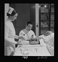 Nurse training. A nurse assists the doctor, who is inserting a needle in a patient's arm prior to a blood transfusion. Sourced from the Library of Congress.