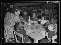 War workers' nursery. A young supervisor at the Bella Vista Nursery School in Oakland, California, eats luncheon with the smallest to prevent dawdling over food. Sourced from the Library of Congress.