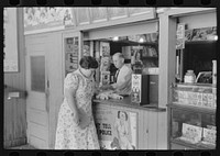 [Untitled photo, possibly related to: Tobacco stand keeper talking with woman. Streetcar terminal, Oklahoma City, Oklahoma] by Russell Lee