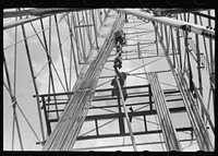 [Untitled photo, possibly related to: Looking up in an oil derrick. Roughneck inserting lengths of pipe into the elevator for pulling the casings. Oklahoma City, Oklahoma] by Russell Lee