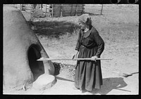 Spanish-American woman testing temperature of earthen oven by determining length of time required to scorch wool, Taos County, New Mexico by Russell Lee