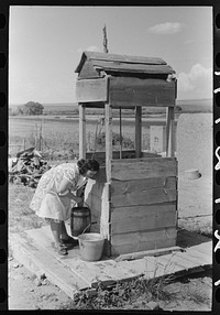 Daughter of Spanish-American farm family drawing water at the well, Taos County, New Mexico by Russell Lee