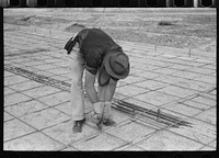 [Untitled photo, possibly related to: Tying iron reinforcement bars together before pouring concrete at migrant camp under construction at Sinton, Texas] by Russell Lee