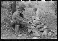 Prospector putting tin can containing his claim deed into his monument on his claim. Pinos Altos, New Mexico by Russell Lee
